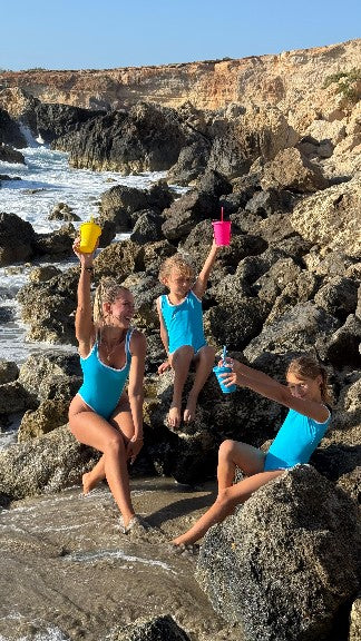 Three children in blue swimsuits play on rocks at the beach, enjoying a sunny day by the water.