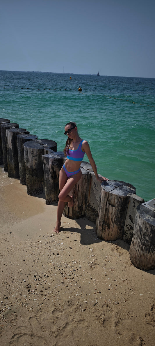 Woman in a bikini sitting on wooden posts by the ocean.