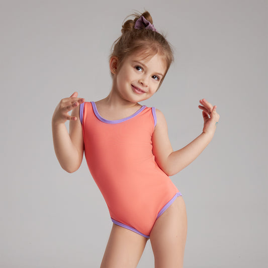  A little girl in a pink bodysuit smiles and poses playfully for the camera.